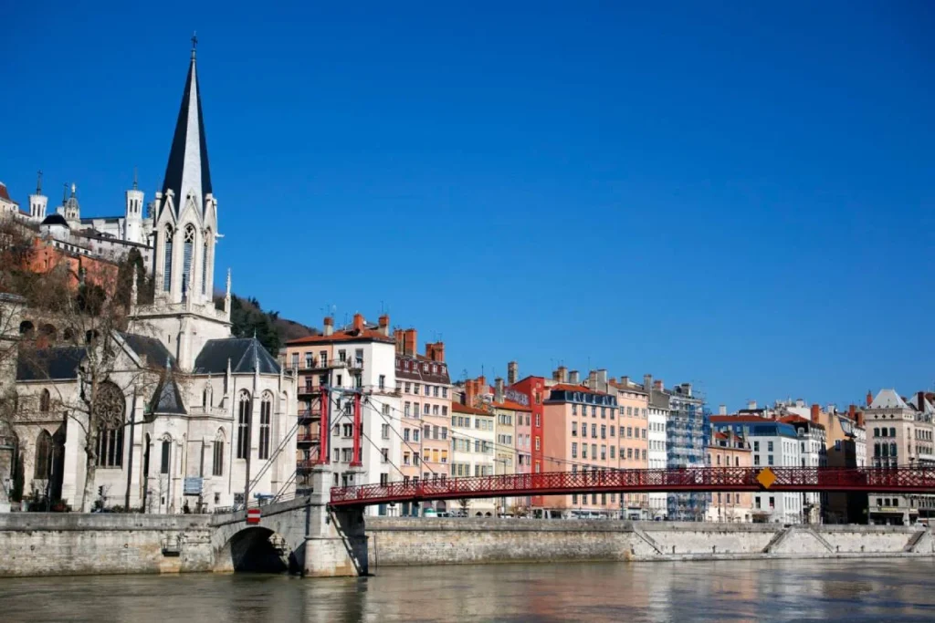 Vue des quais de la Saône à Lyon avec l’église Saint-Georges et la passerelle Saint-Georges sous un ciel bleu.