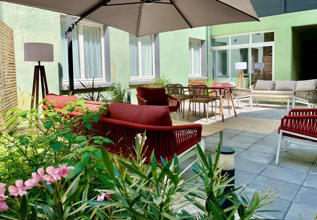 Terrasse extérieure de l’Hôtel Villa Berlioz à Lyon, avec mobilier confortable, parasol et végétation.