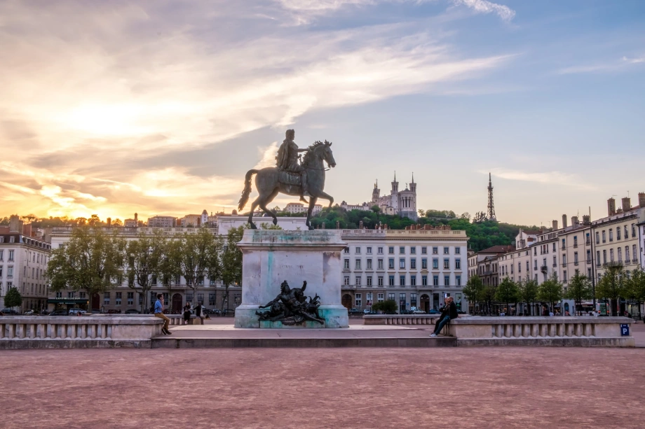 Statue équestre de Louis XIV sur la place Bellecour à Lyon au coucher du soleil, avec la basilique de Fourvière en arrière-plan