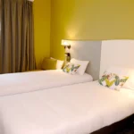 Chambre triple de l’Hôtel Villa Berlioz à Lyon avec deux lits simples, déco moderne et éclairage chaleureux.