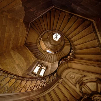 Ornate helical stone staircase with wrought iron railing seen from above, inside a historic building on Fourviere hill in Lyon