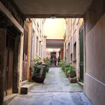 Narrow traboule passageway in Lyon's Croix-Rousse district, lined with old stone buildings and potted plants