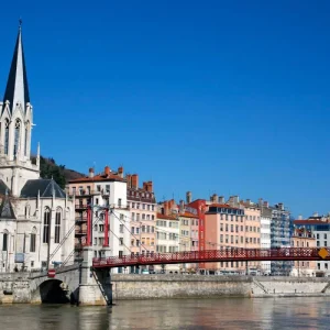 Vue des quais de la Saône à Lyon avec l’église Saint-Georges et la passerelle Saint-Georges sous un ciel bleu.
