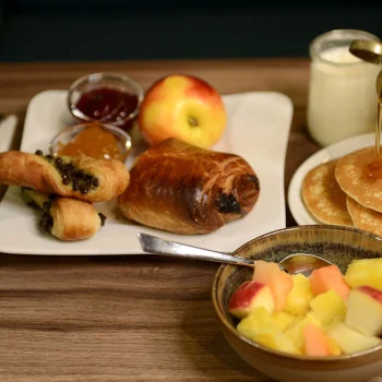 Breakfast at Villa Berlioz Hotel in Lyon featuring pastries, fresh fruit, pancakes with syrup and drinks.