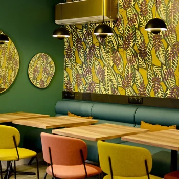 Salle petit-déjeuner de l’Hôtel Villa Berlioz à Lyon avec décoration moderne, miroirs ronds et chaises colorées.